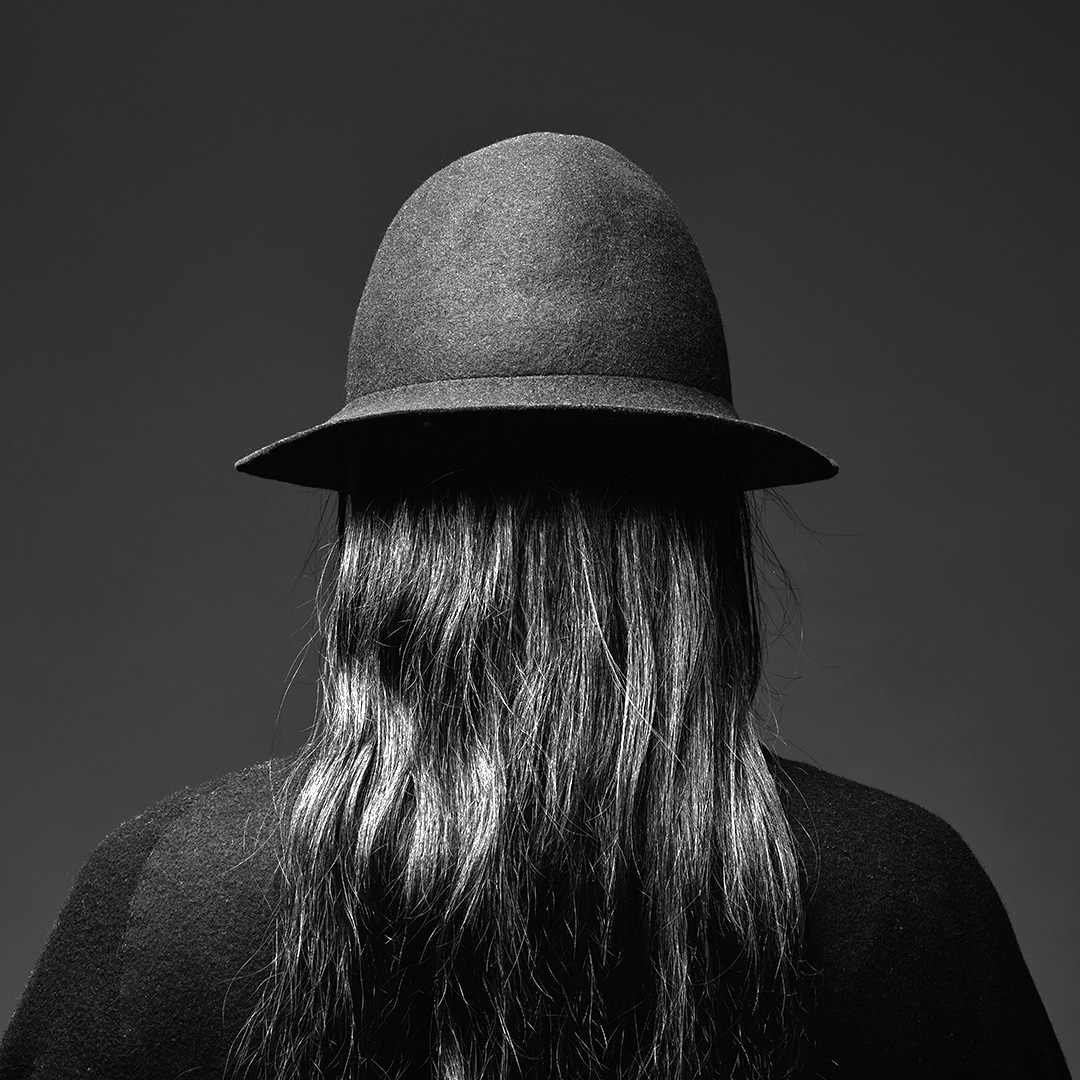 Black and white photo of a person with long hair and hat on, photographed from the back
